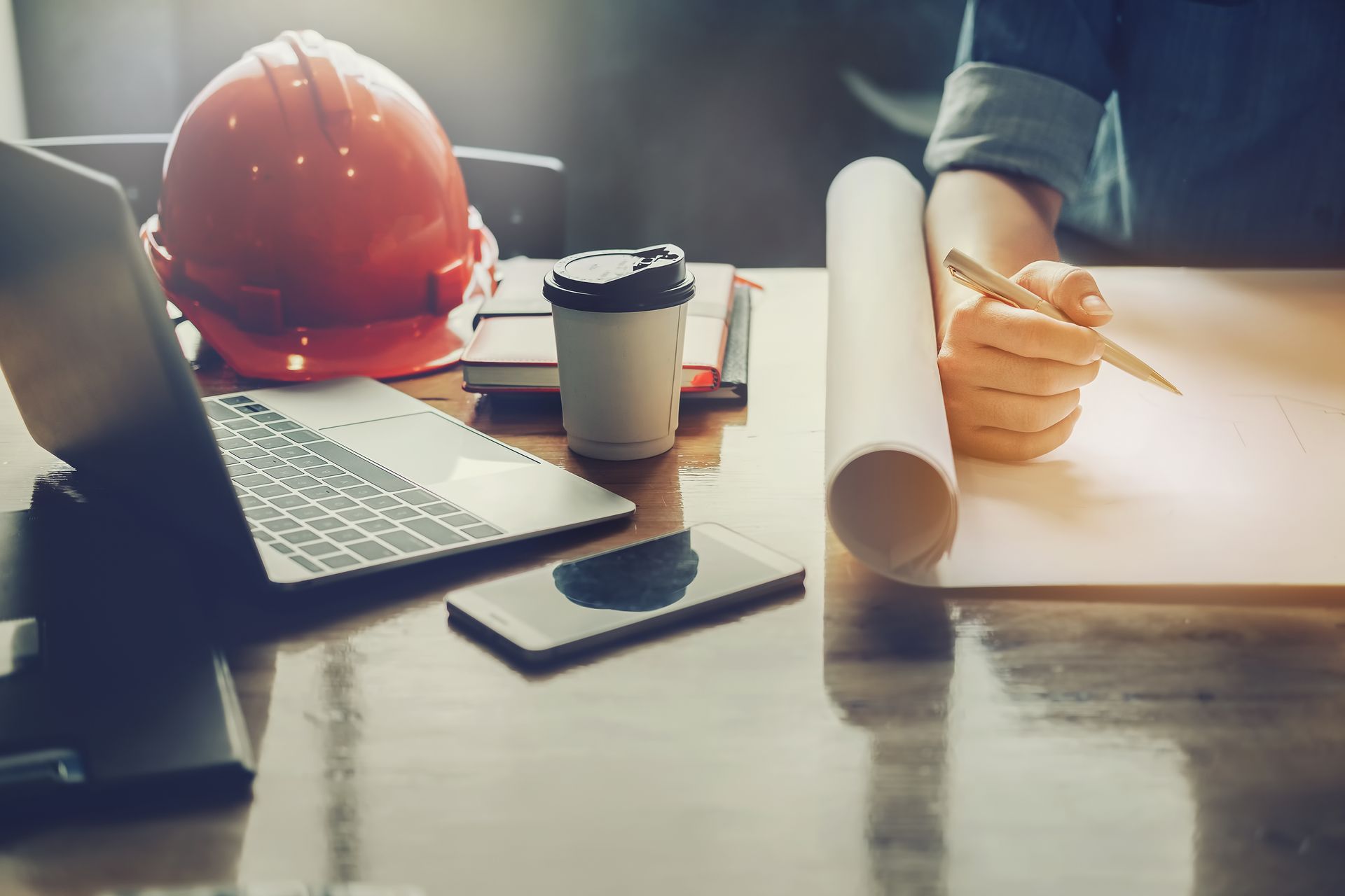 A person is sitting at a desk with a laptop and a hard hat.