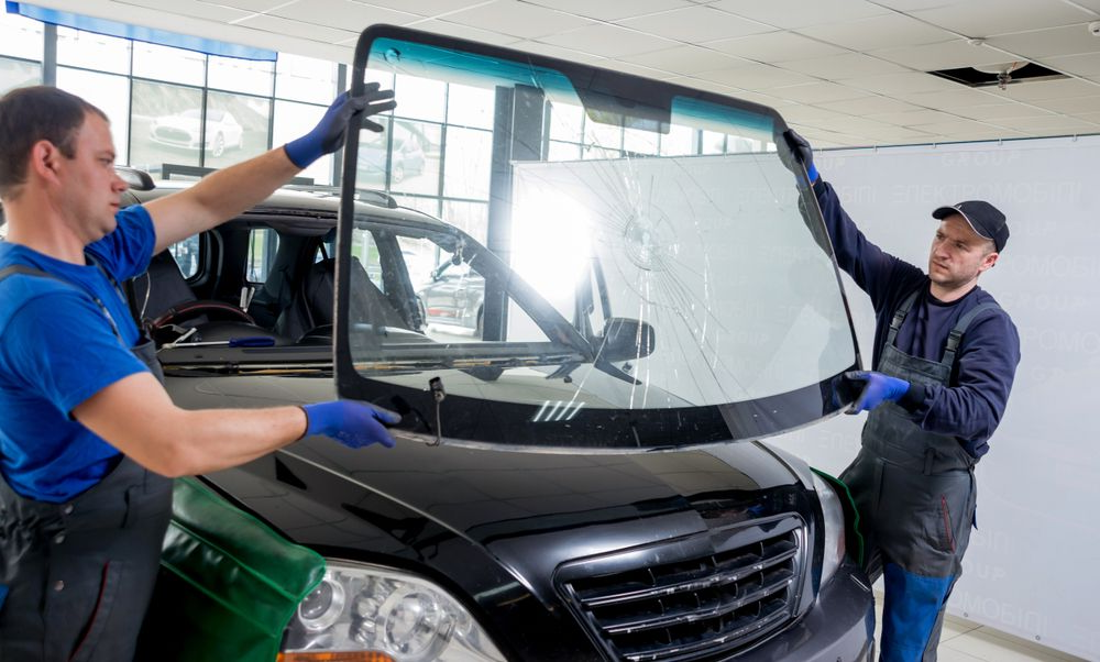 Two Workers Installing a Windshield on a Black Car in a Garage — Southern Tablelands Windscreen Repairs in Goulburn, NSW