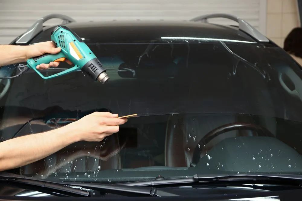 Hands Applying Window Tint to a Car Windshield With a Heat Gun — Southern Tablelands Windscreen Repairs in Moss Vale, NSW