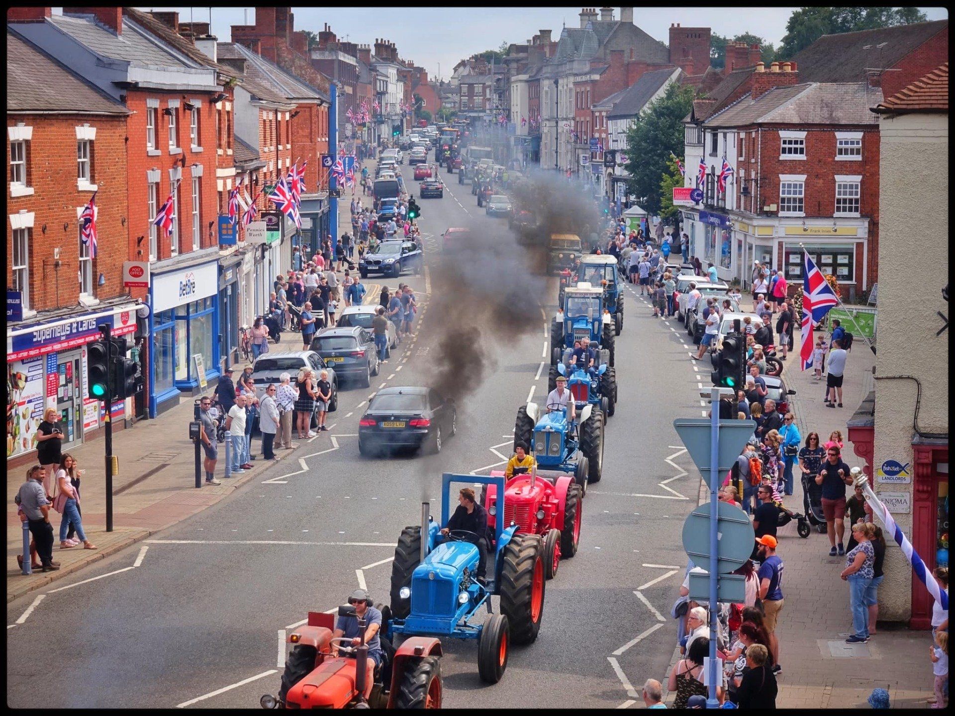 A row of tractors are driving down a city street