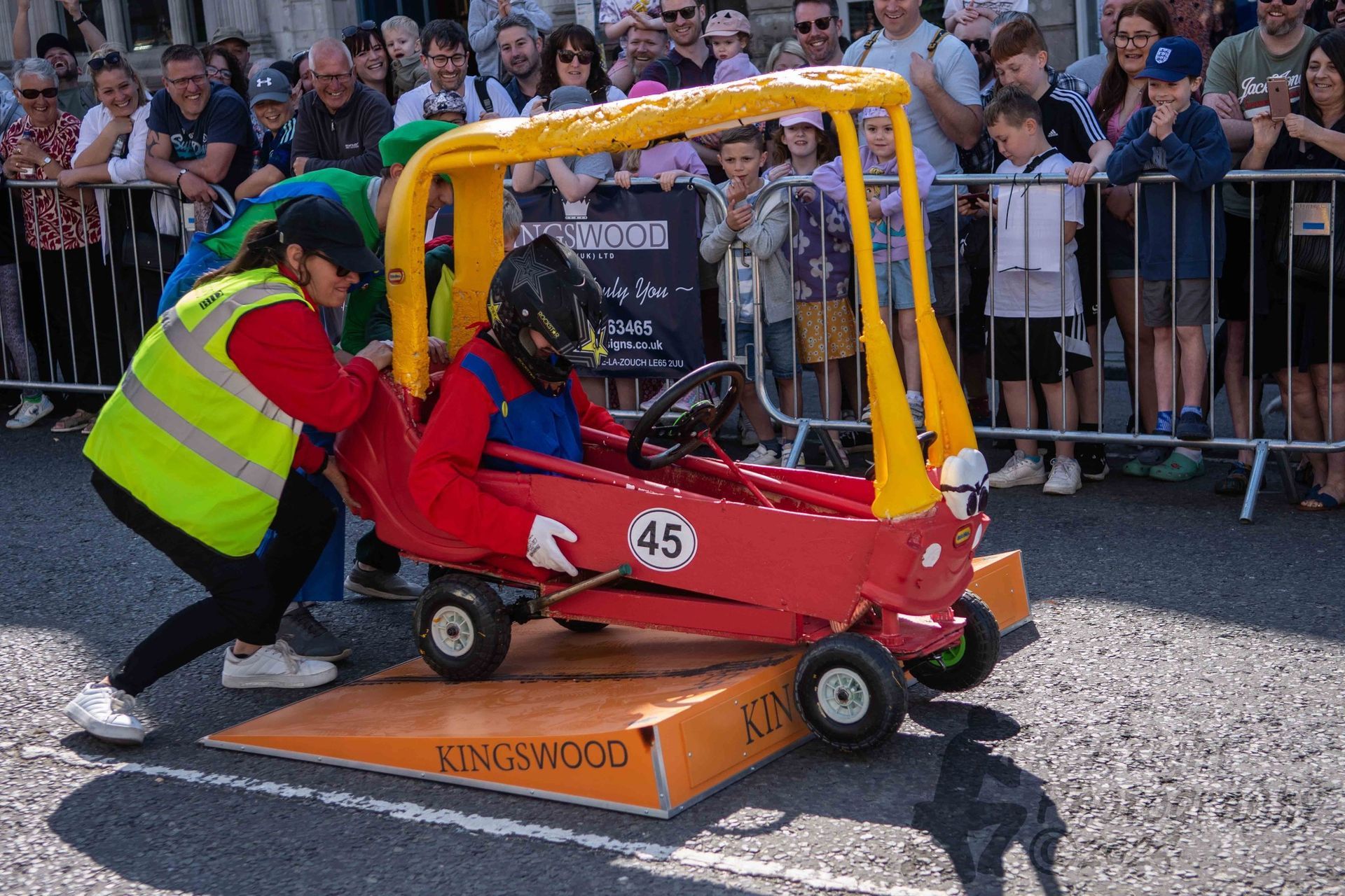 A group of people are pushing a red and yellow toy car down a ramp.