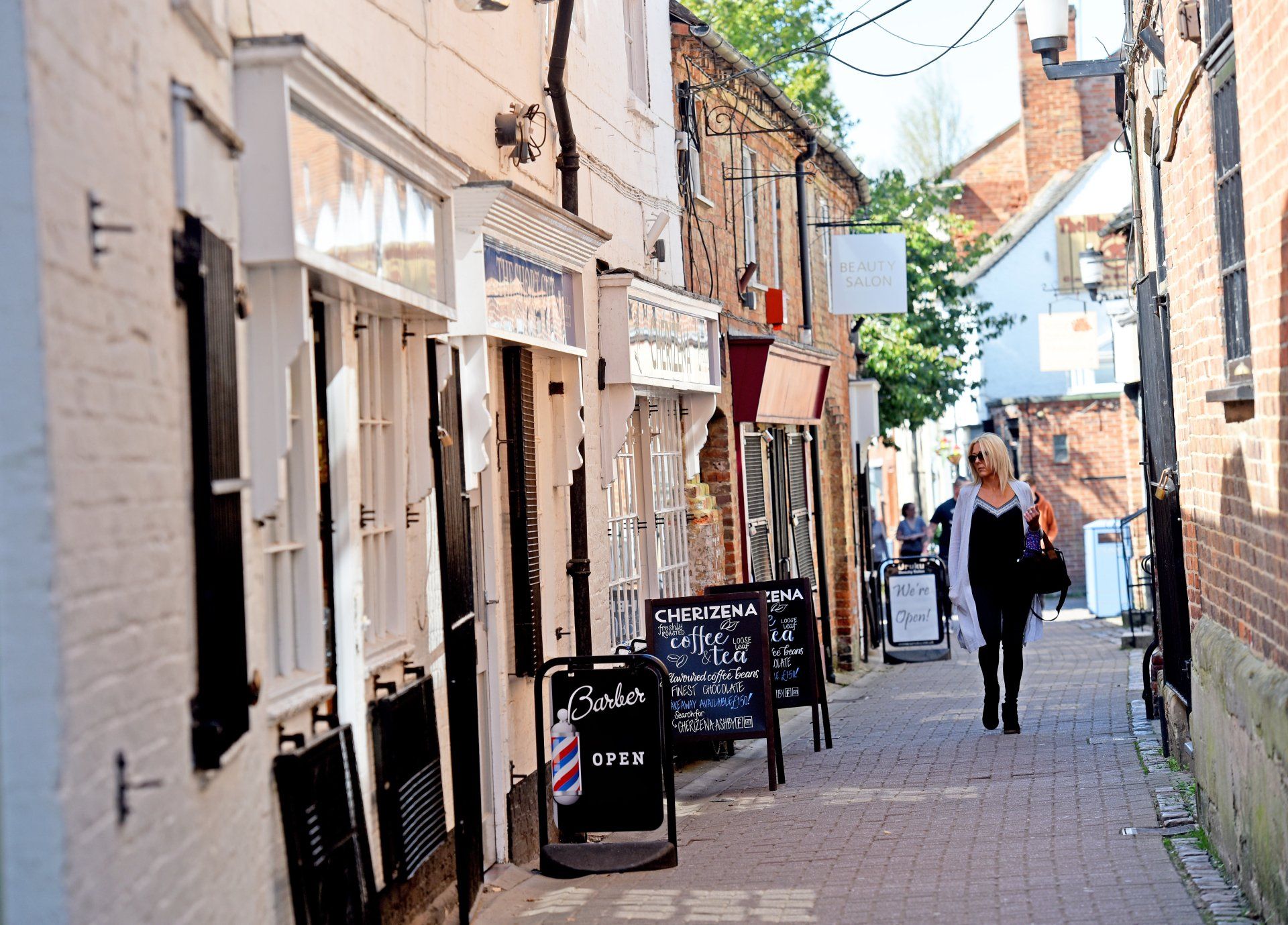 A woman is walking down a narrow alleyway between two buildings.