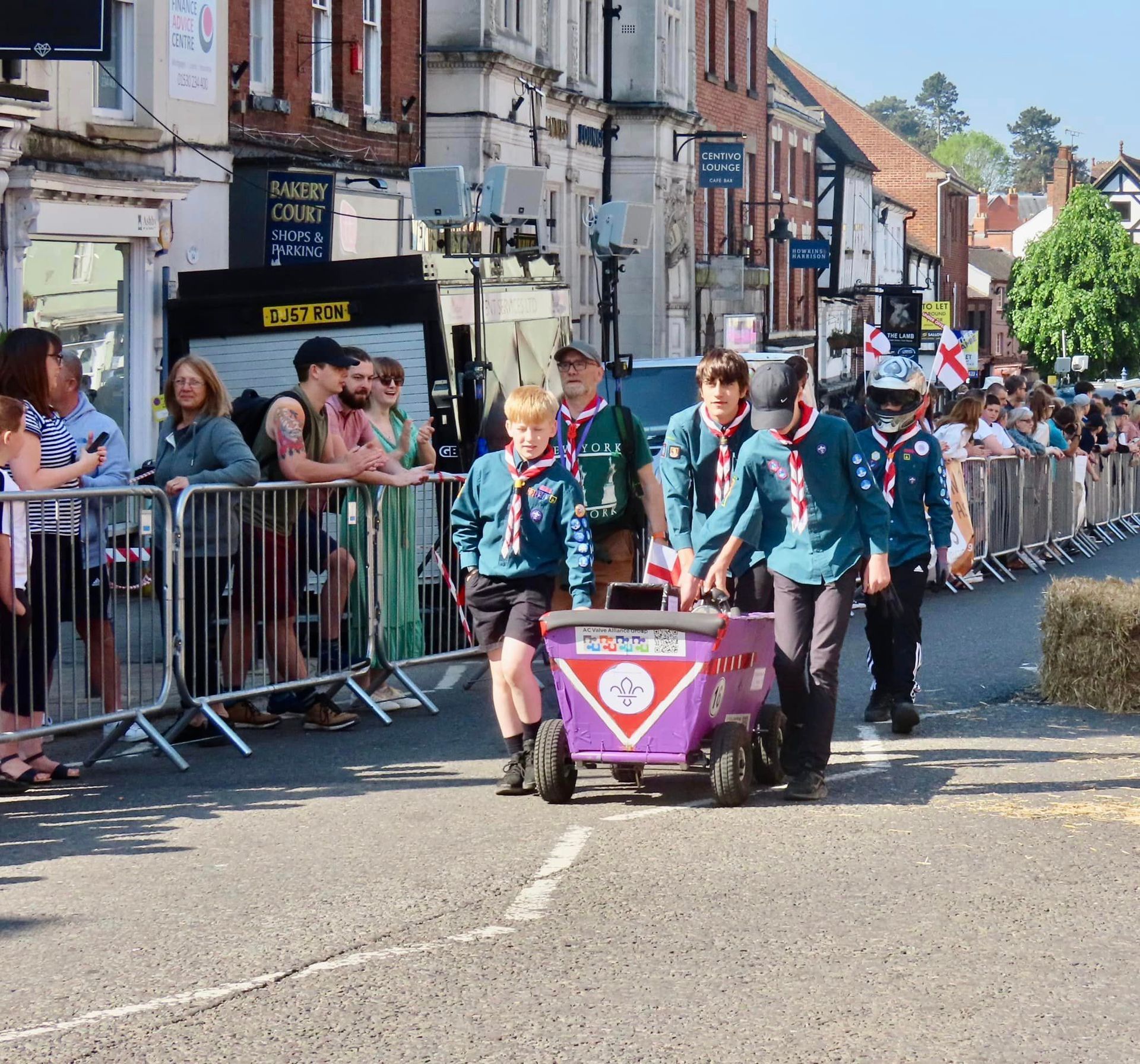 A group of boy scouts push a purple cart down a street