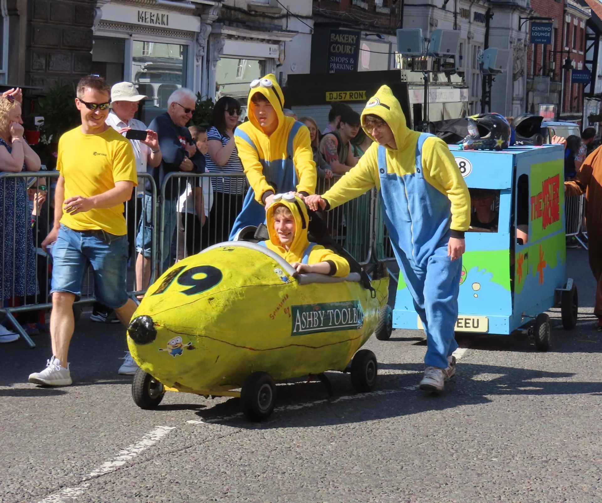 A group of people dressed as minions are driving a yellow car with the number 19 on it.