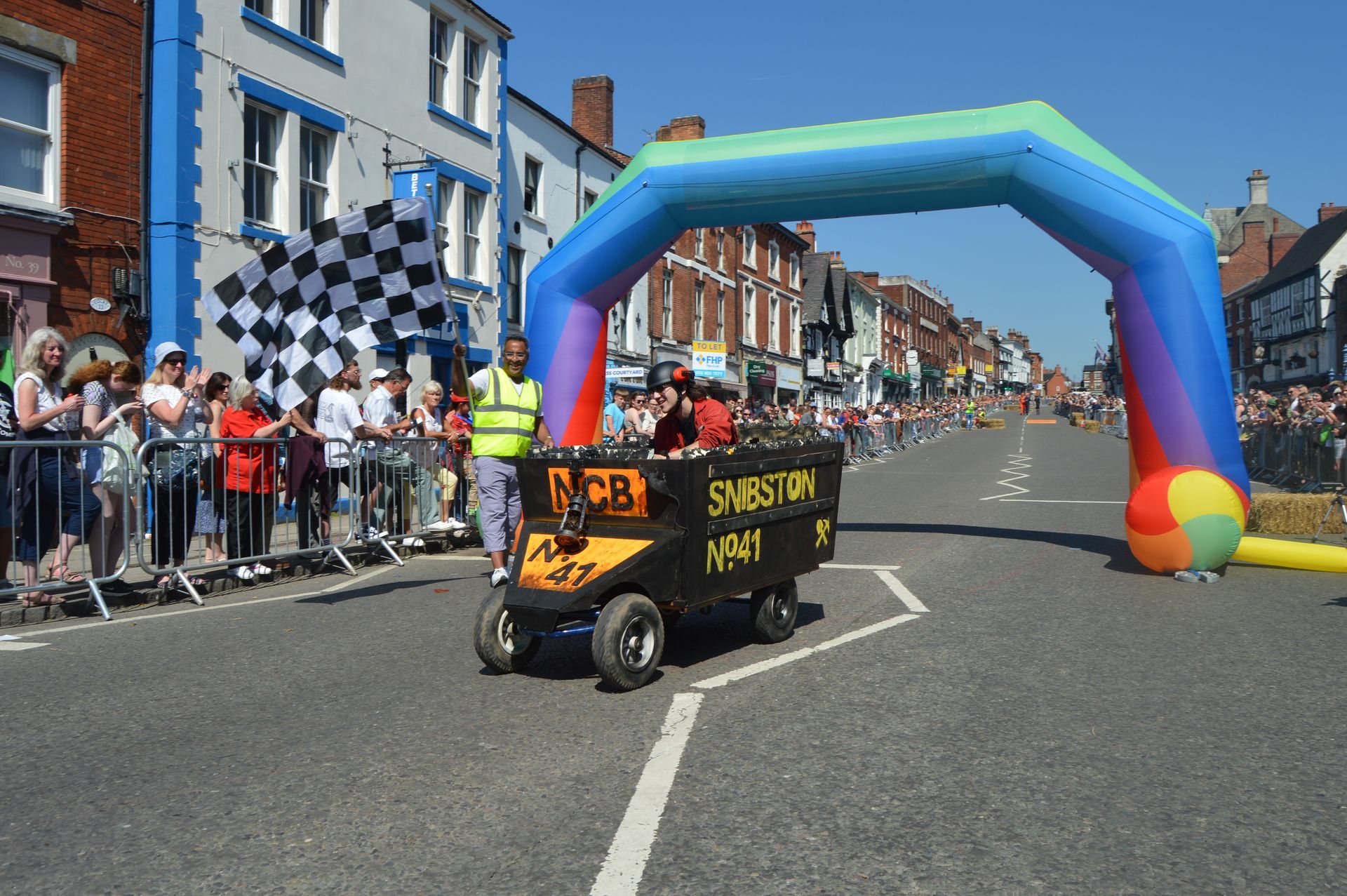 A person is driving a cart down a street with a checkered flag in the background.