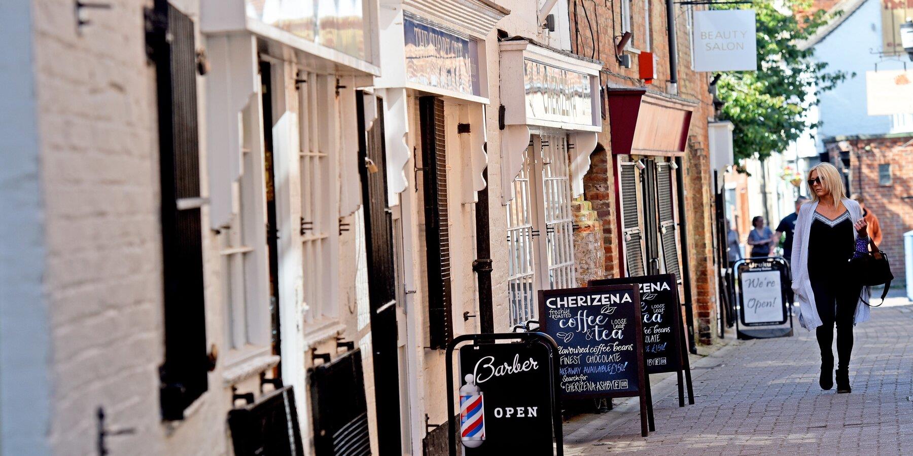 A woman is walking down a narrow street lined with shops.