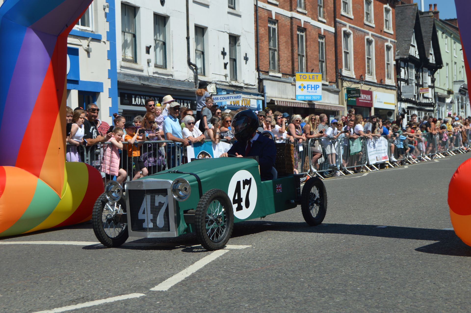 A green car with the number 47 on it is driving down a street.