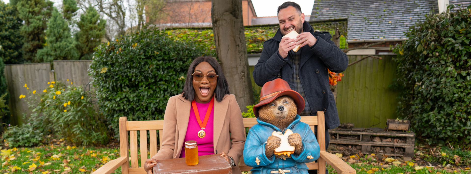 A man and a woman are sitting on a bench next to a paddington bear statue.