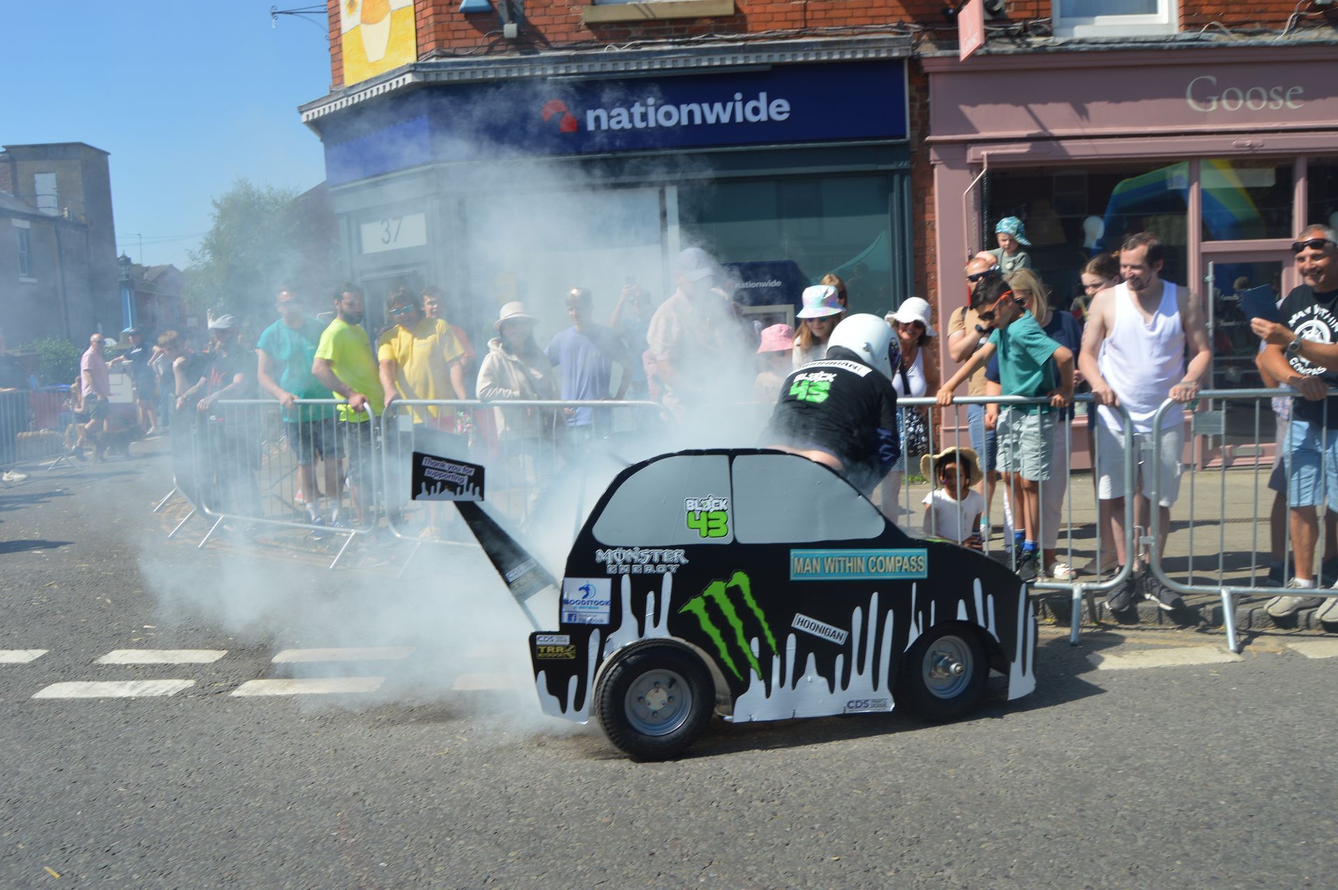 A small car is driving down a street with smoke coming out of it.