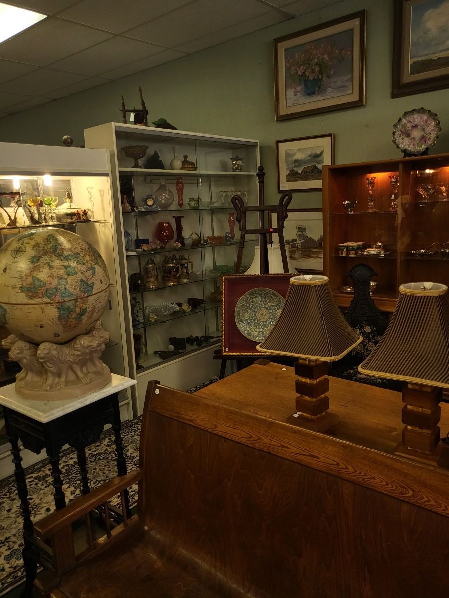 Antique shop interior, showcasing furniture, decor, and a glass display cabinet filled with collectibles and framed paintings.