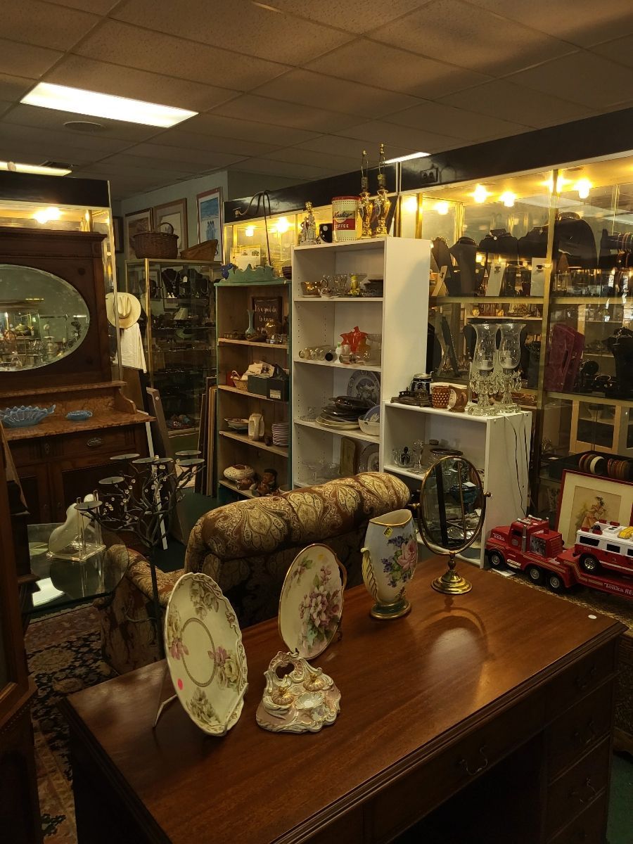 Antique shop interior with display cases, shelves of items, a table with pottery, and a couch.