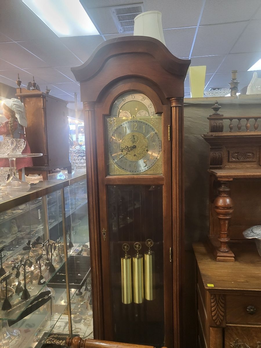 Tall wooden grandfather clock with brass face and gold pendulums.