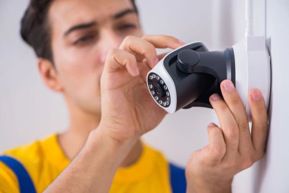 Una persona installa una telecamera di sicurezza nera su una parete con un cacciavite.