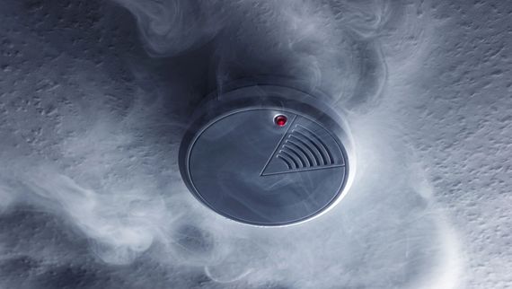 Rivelatore di fumo rotondo con LED rosso sul soffitto, circondato da un vortice di fumo