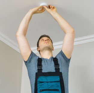 Una persona in tuta blu si allunga per installare un apparecchio di illuminazione a soffitto.