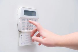 Mano che preme i pulsanti su una tastiera di sicurezza bianca montata a parete, dotata di piccolo display e pannello aperto.