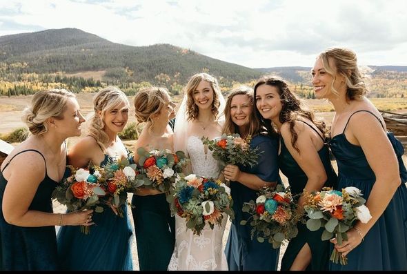 Bride and bridesmaids with colorful bouquets in a mountain setting. They are smiling and wearing teal dresses.