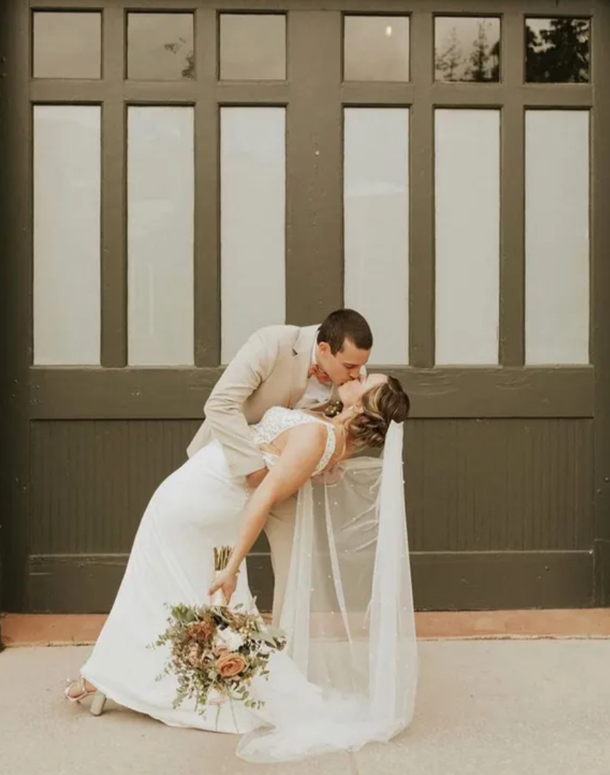 Woman with short, textured black hair styled with flower hairpiece; wearing a light jacket, and long earrings.