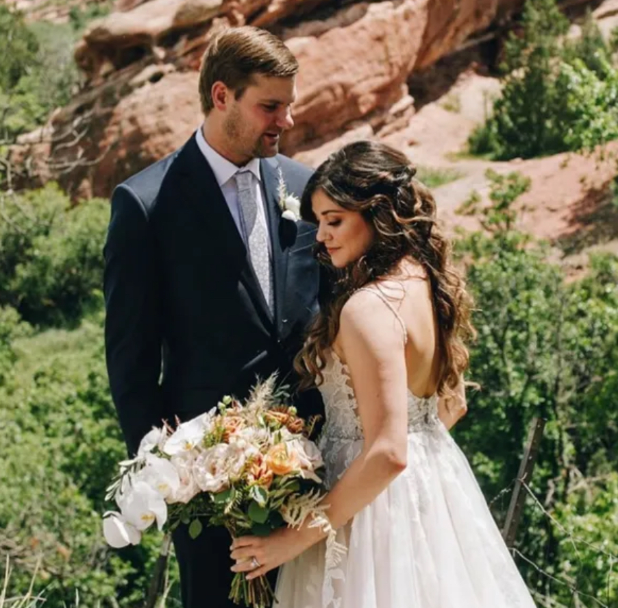 Wedding couple in outdoor setting. Bride in white dress holds bouquet; groom in suit.