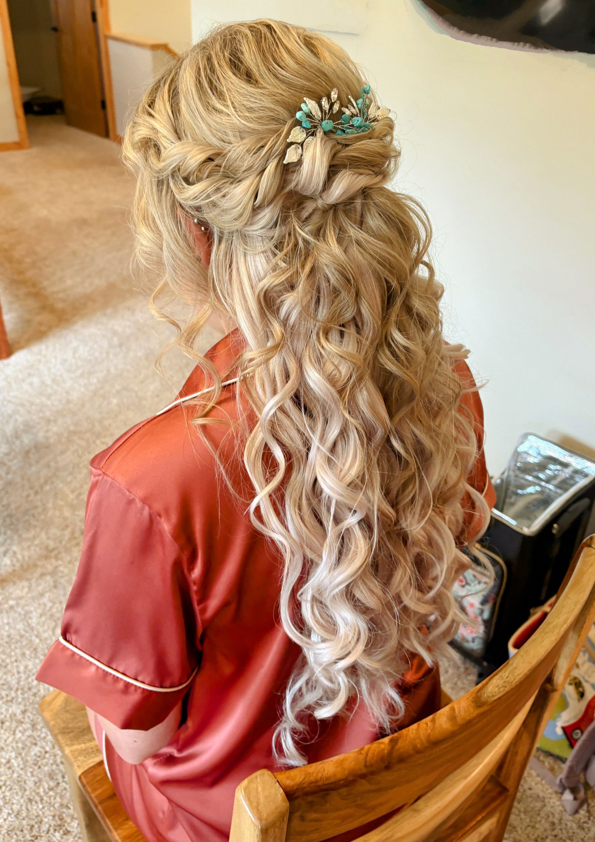 Bride in a white lace dress with curly hair looks at a groom in a navy suit and red tie, outdoors.