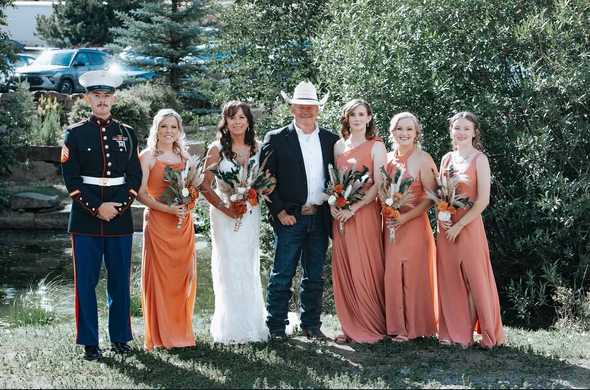 Bride facing bridesmaids in lavender dresses; holding hands in front of a fireplace.