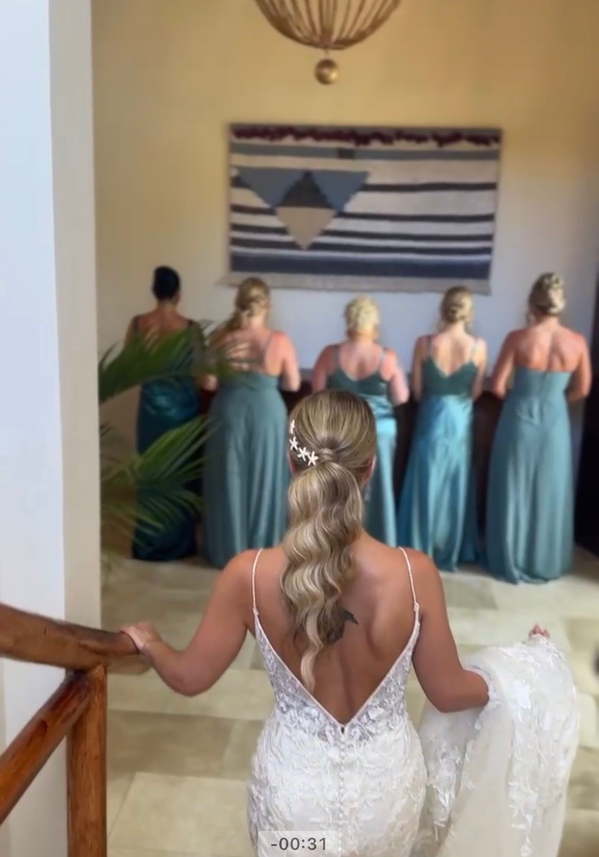 Bride descending stairs with bridesmaids in teal dresses.