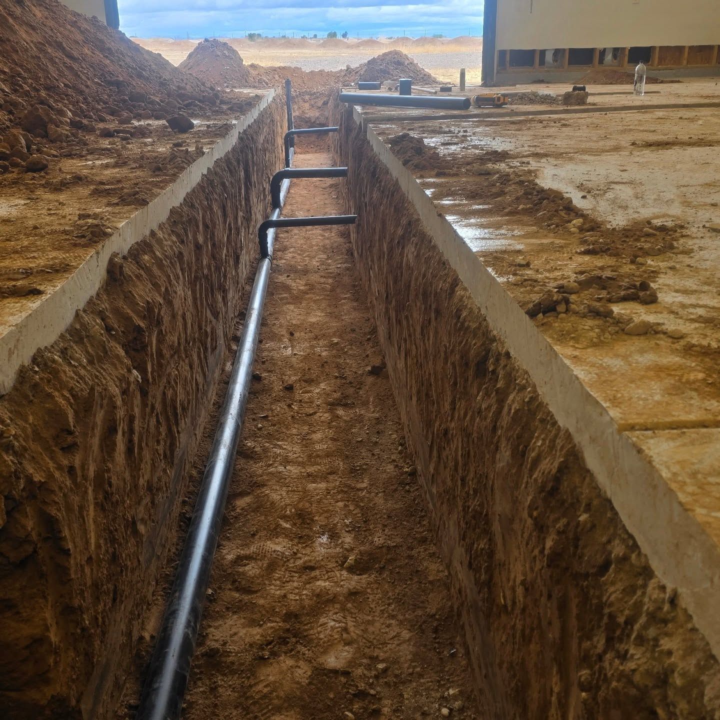 A trench with pipes going through it and a building in the background