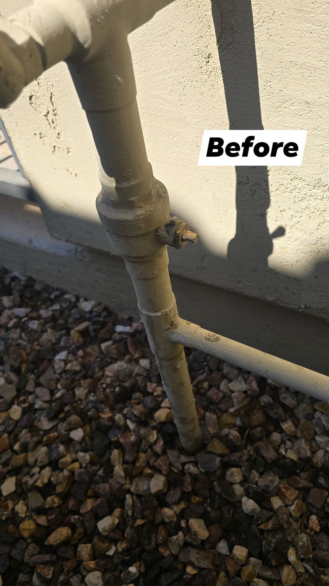 A pipe is sitting on top of a pile of gravel next to a wall.