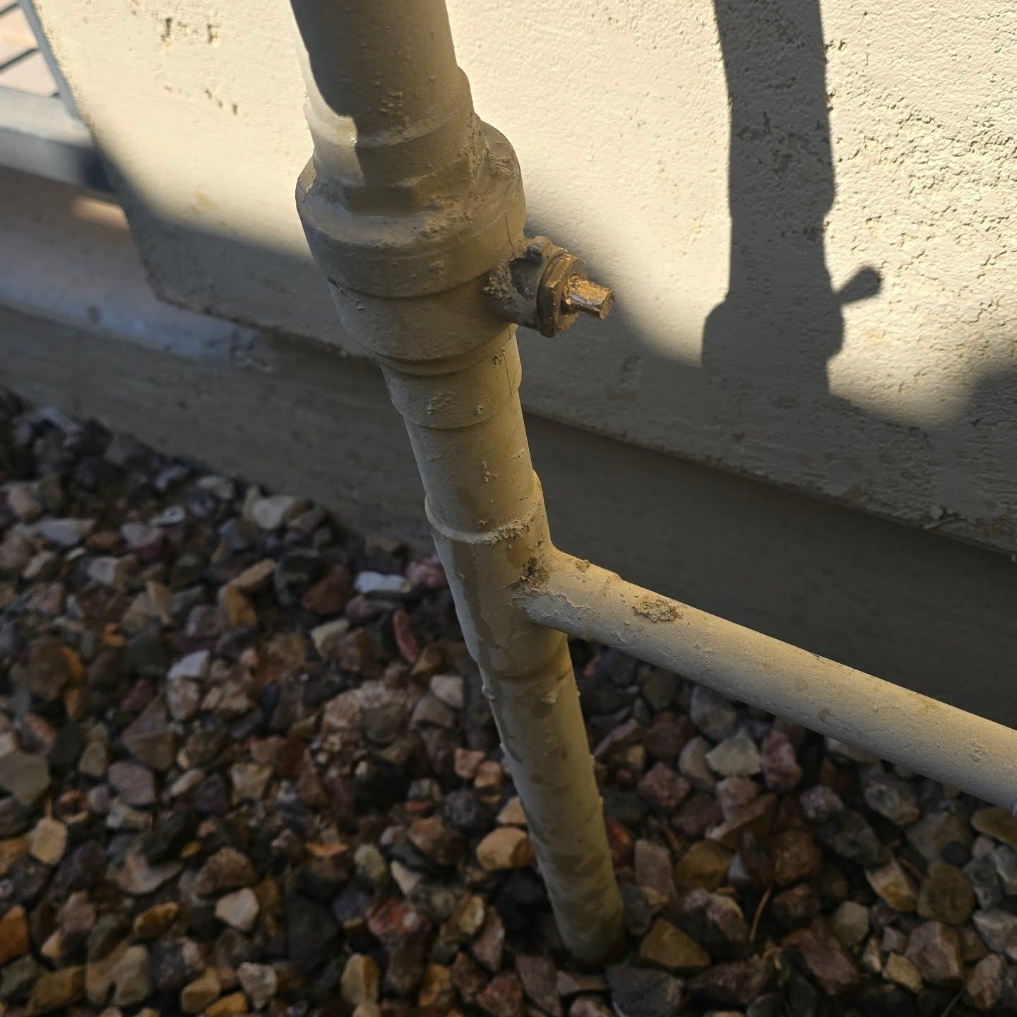 A pipe is sitting on a pile of gravel next to a wall.