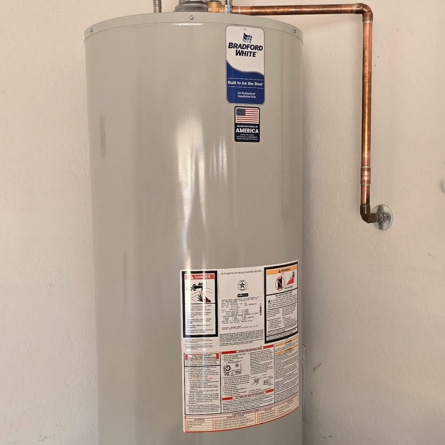 A water heater is hanging on a wall next to a copper pipe.