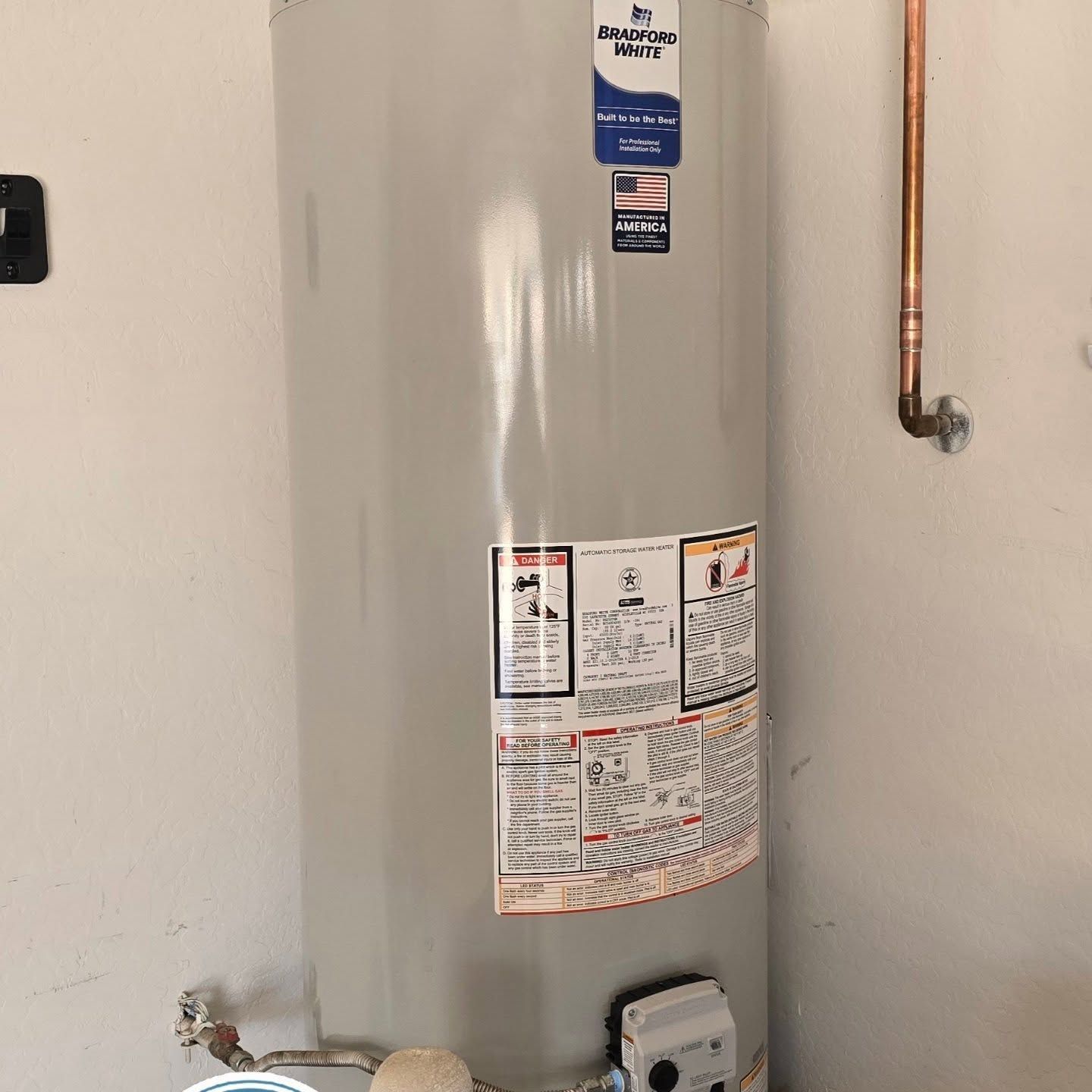 A water heater is sitting on a wall next to a copper pipe.
