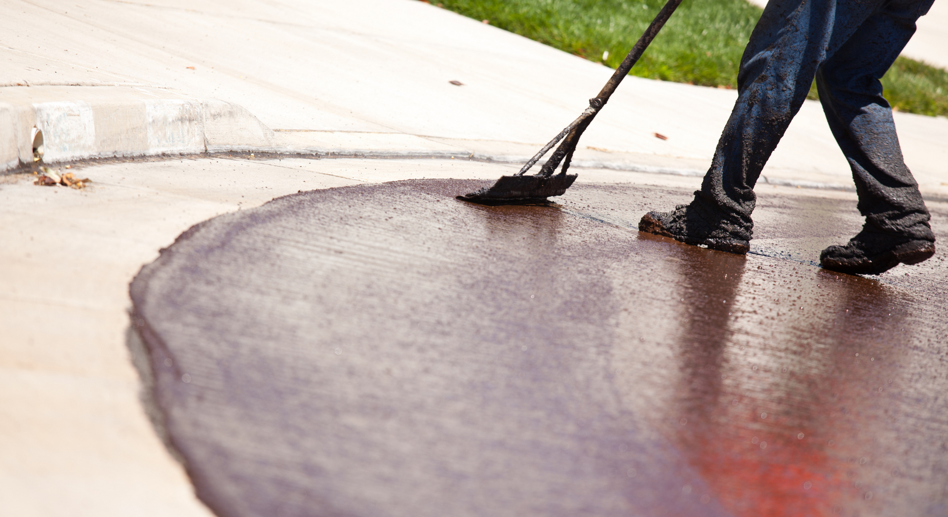 A person is spreading asphalt on a sidewalk with a broom.