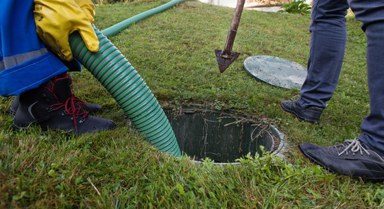 A man is pumping water into a septic tank with a hose.