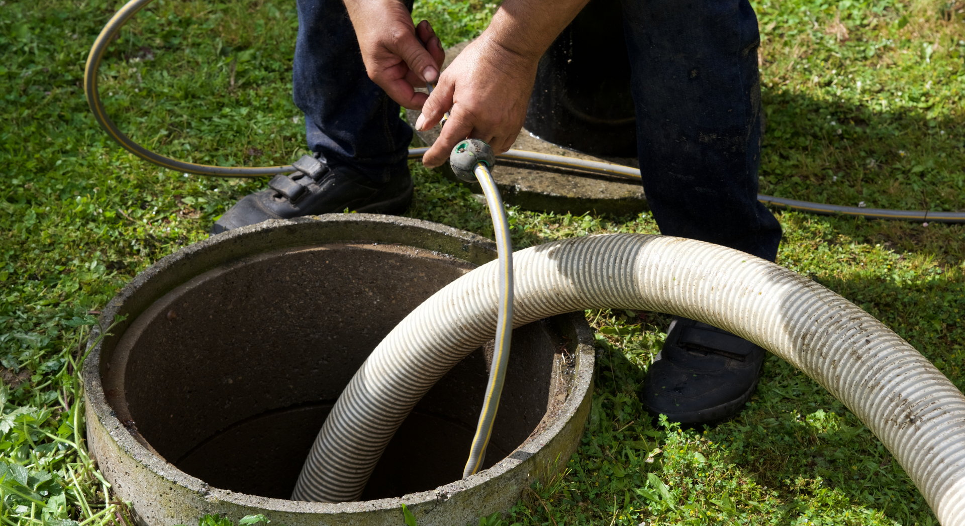 A man is pumping a hose into a septic tank.