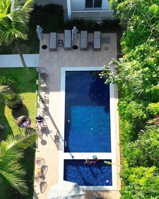 Vista aérea de uma piscina azul ao lado de espreguiçadeiras e vegetação exuberante, com uma piscina menor abaixo.