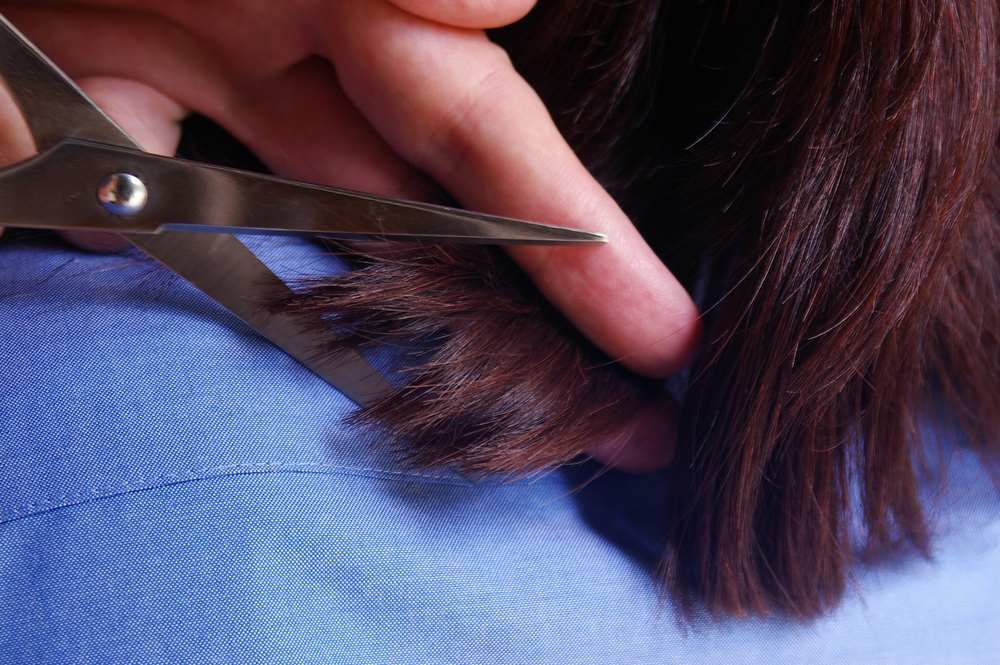 A Woman is Cutting Her Hair With Scissors — Embellish Hair and Beauty In Slade Point, QLD