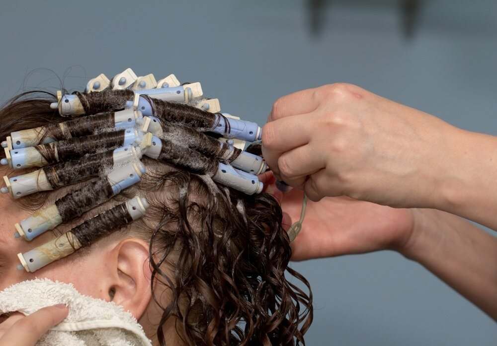 A Woman is Getting Her Hair Curled by a Hairdresser — Embellish Hair and Beauty In Slade Point, QLD