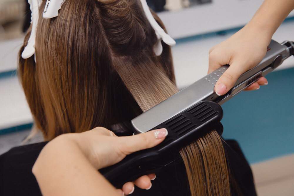 A Woman is Getting Her Hair Straightened by a Hairdresser — Embellish Hair and Beauty In Slade Point, QLD