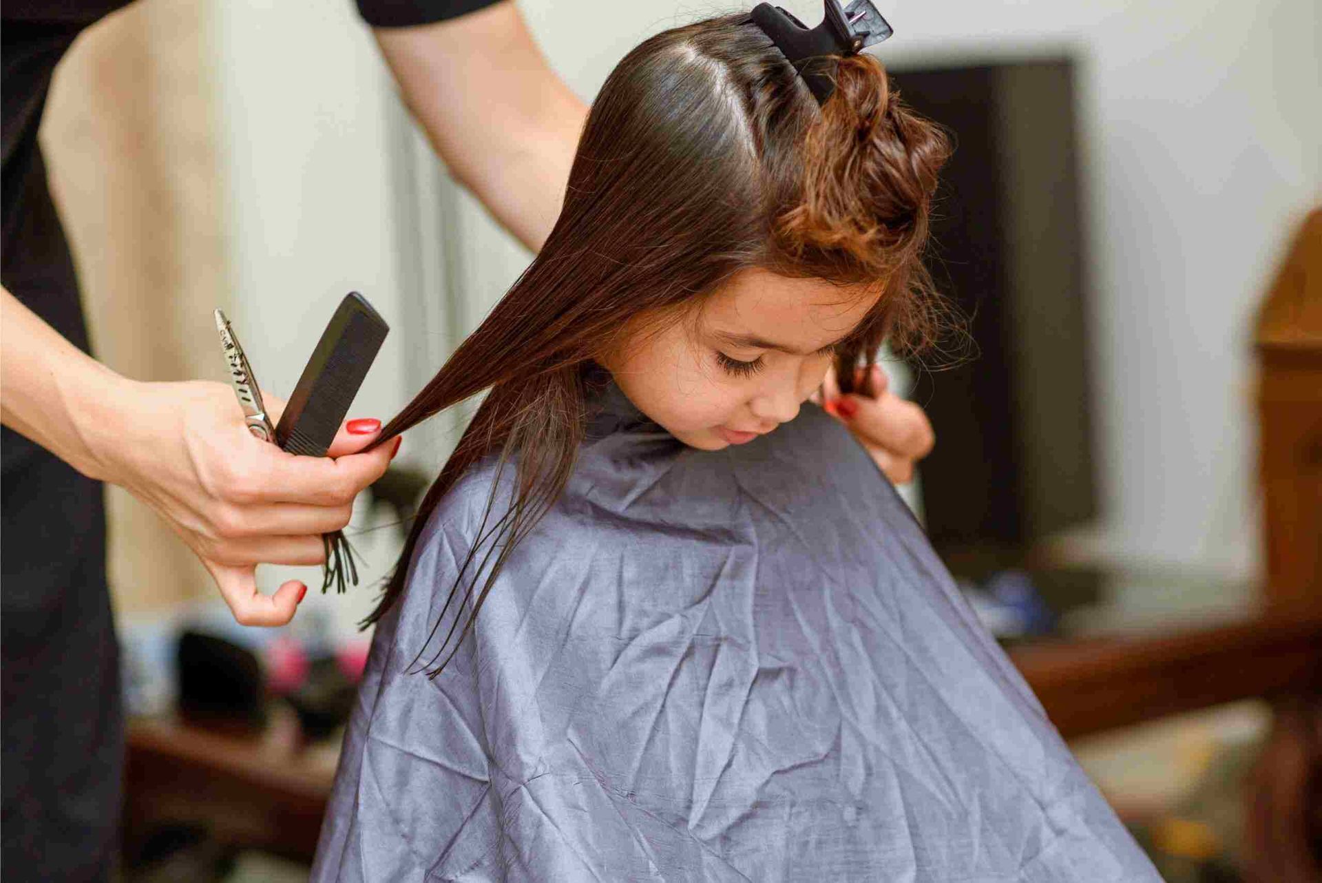 A Little Girl is Getting Her Hair Cut by a Hairdresser — Embellish Hair and Beauty In Slade Point, QLD
