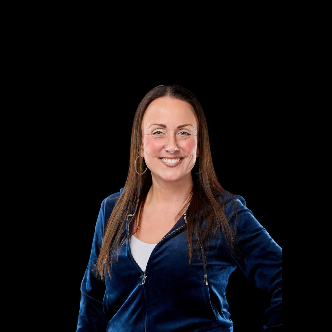Joan Lenahan, Owner & Business Manager  in a blue jacket is smiling in front of a black background.