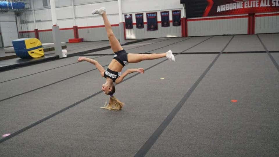 A cheerleader is doing a handstand on a gym floor.