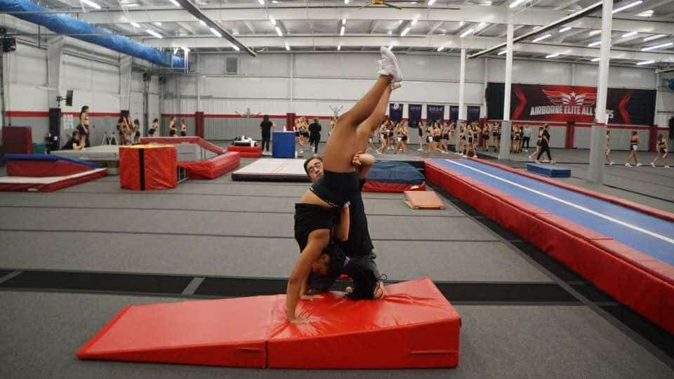 A woman is doing a handstand on a red mat in a gym.