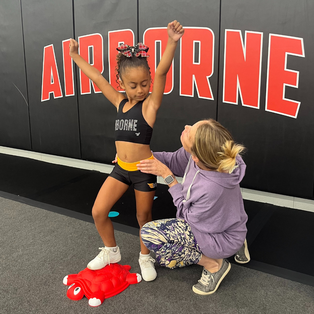 A little girl is standing in front of a wall that says airborne