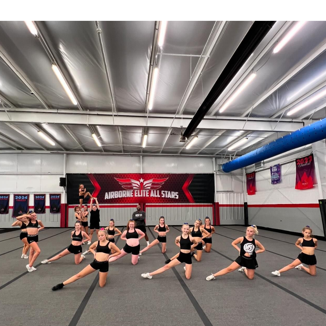 A group of cheerleaders are doing stretching exercises in a gym