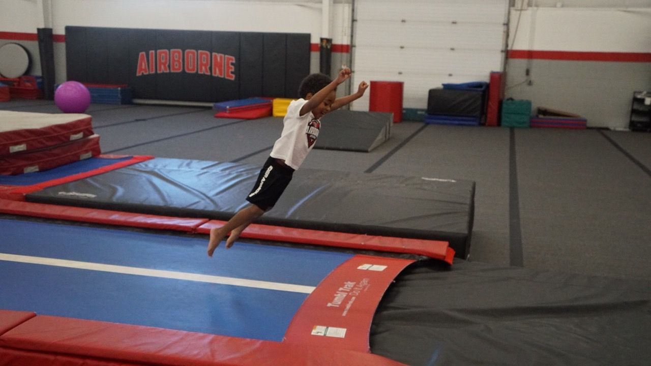 A young boy is jumping on a trampoline in a gym