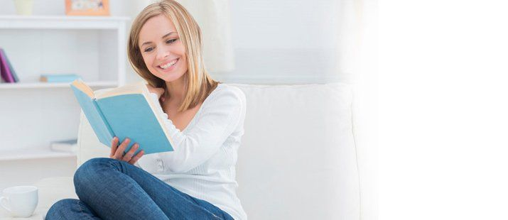 A woman is sitting on the floor reading a book.