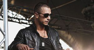 A man wearing sunglasses and a leather jacket is standing on a stage.