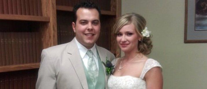 A bride and groom are posing for a picture in front of a bookshelf.