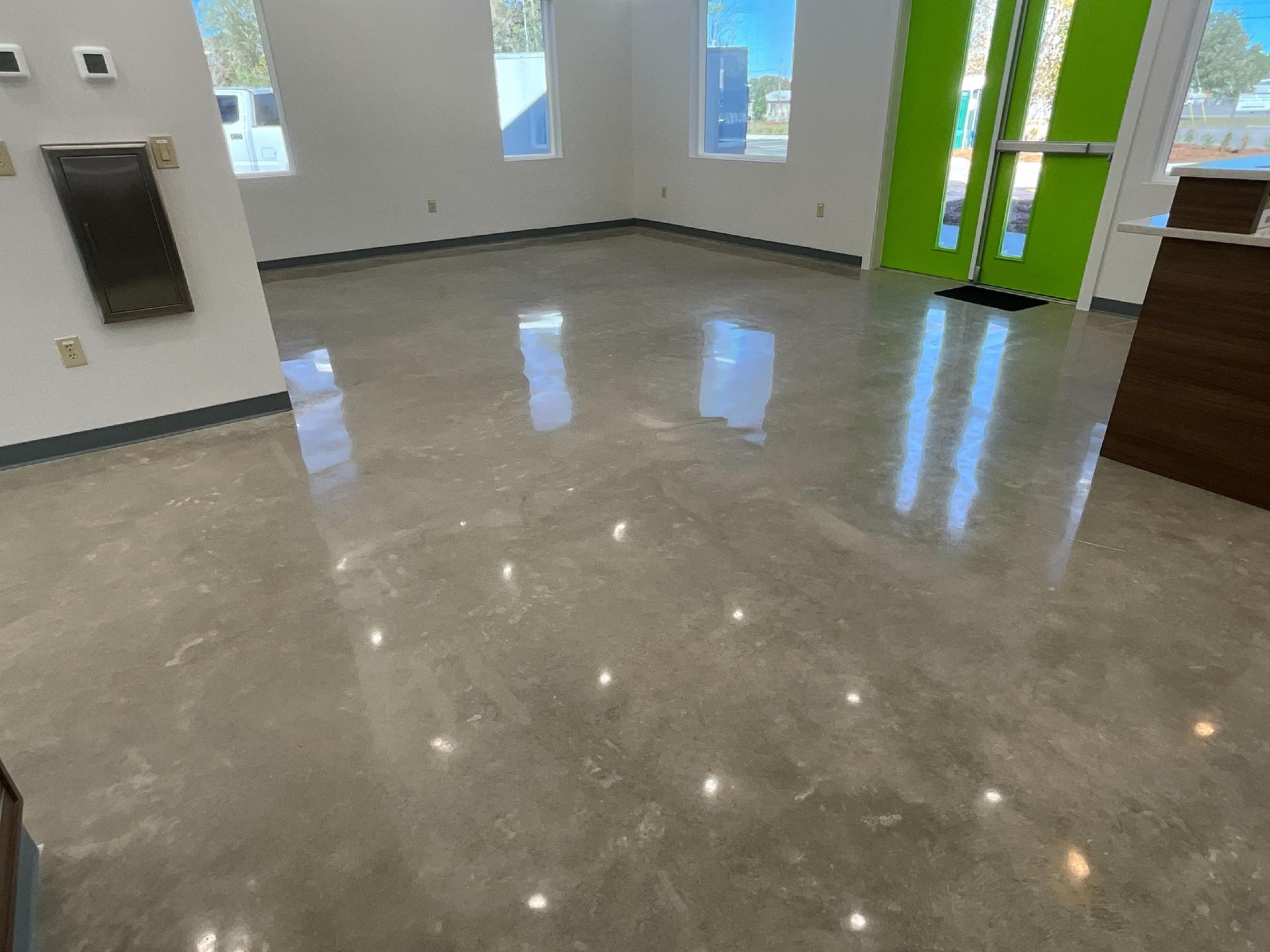 Polished concrete floor in an empty room, reflecting light. Walls are white with a green door.