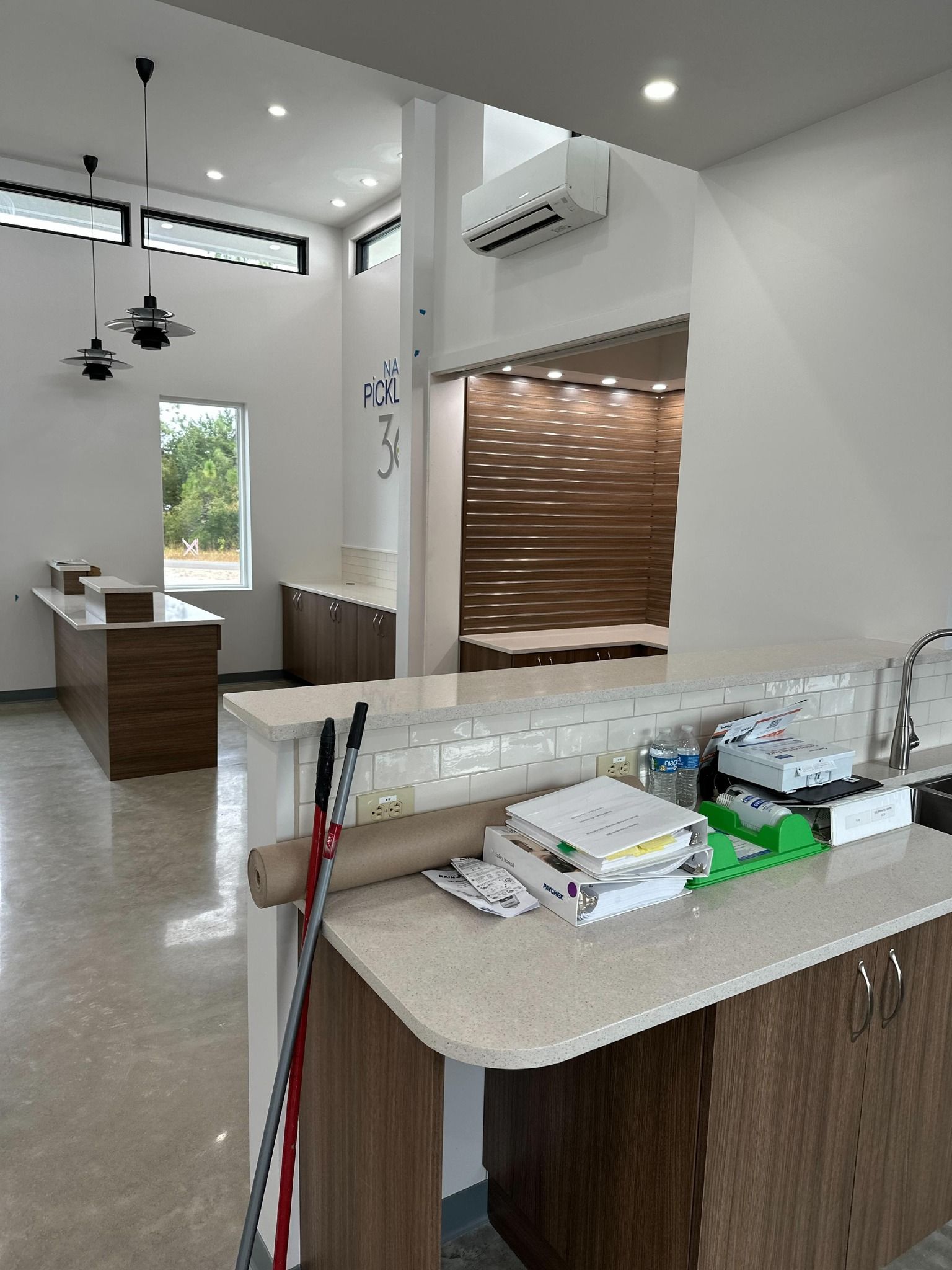 Interior view of a bright, modern space with a reception desk, waiting area, and wooden accents. Includes an air conditioner and a window.